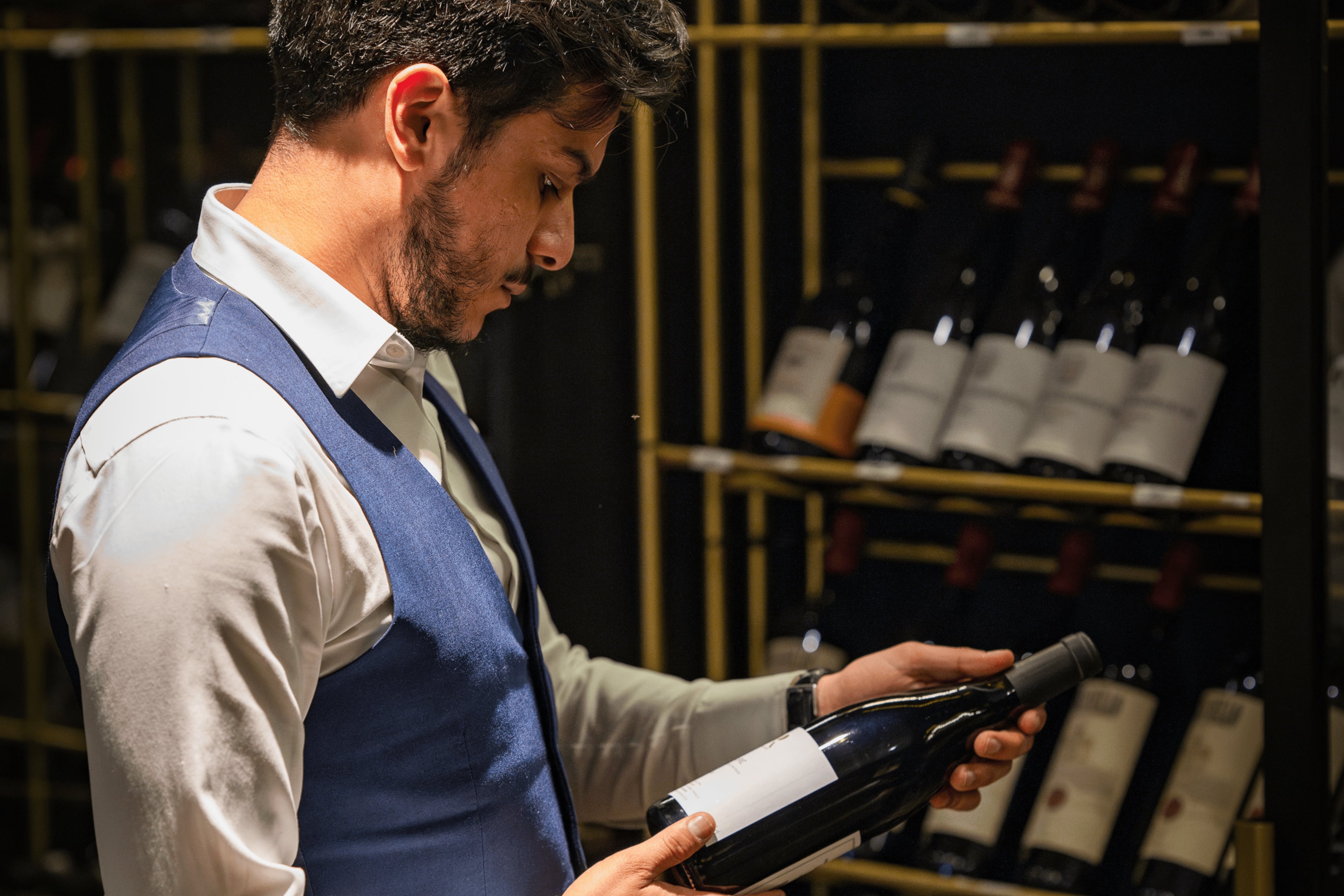 A waiter holds a wine bottle in front of an elegant wine display in The Wine Room, perfect for intimate gatherings and wine tasting